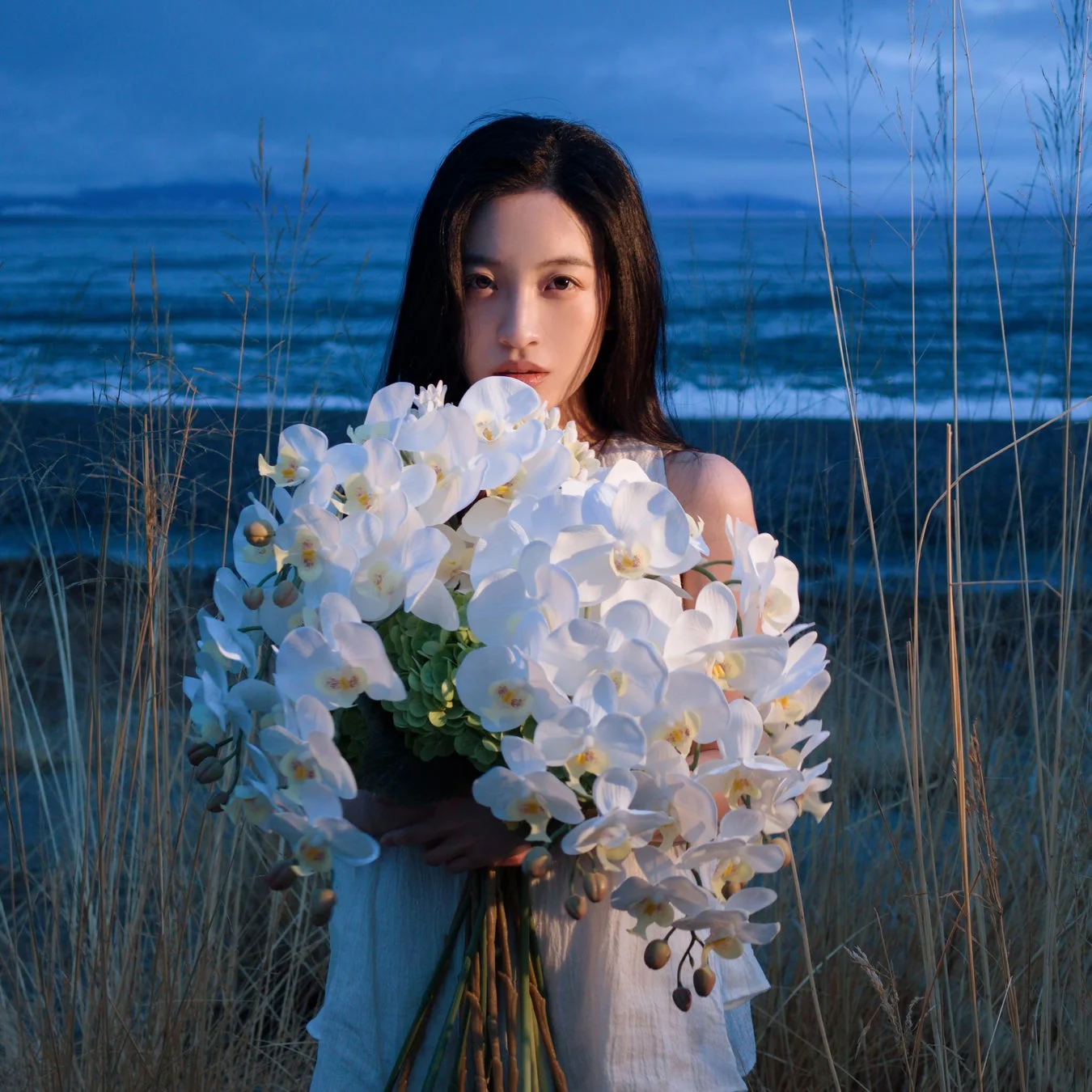 夕暮れの海辺で花束を抱える女性