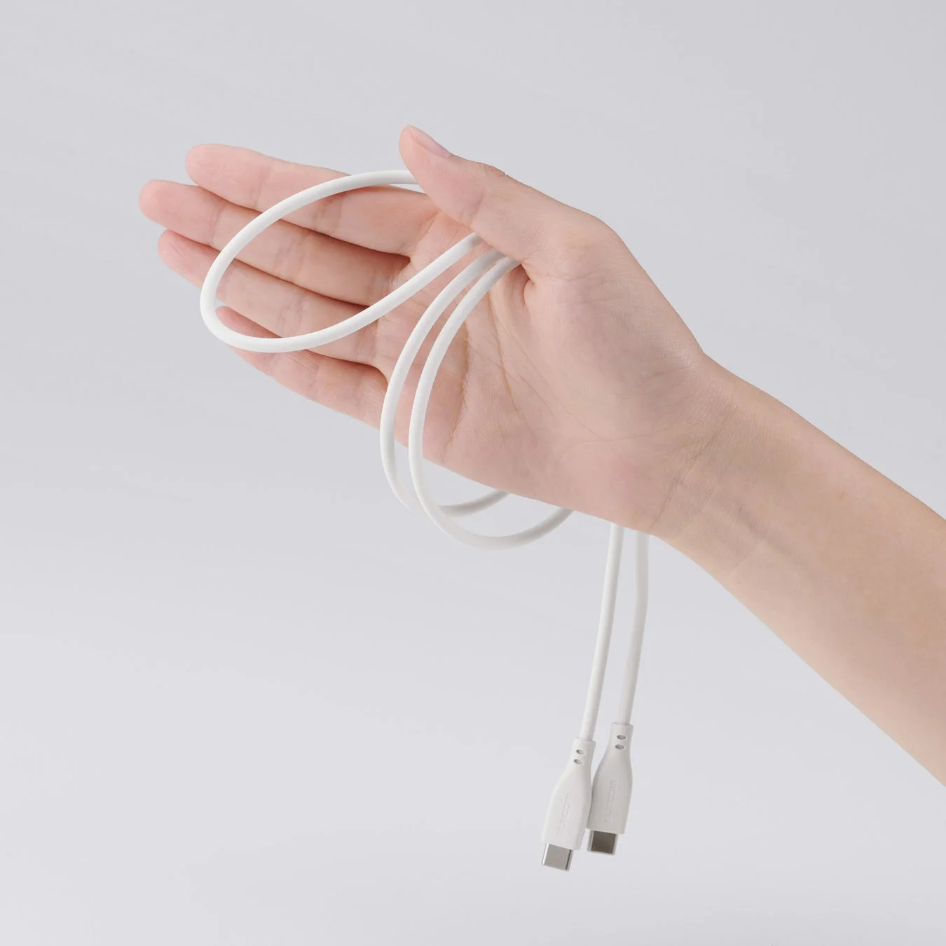 白い背景の前で、白いUSB-Cケーブルを片手が優しく持っている様子を捉えた画像です