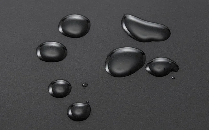 暗い背景の上に様々な大きさの透明な水滴が多数散らばっている様子を捉えた画像です。水滴の丸い形状が表面張力を示唆しています。