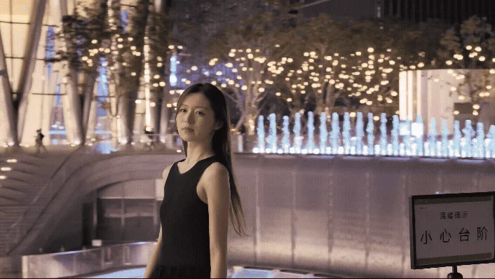 夜の都会でライトアップされた噴水を背景に立つ女性