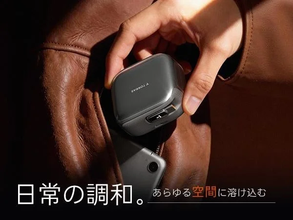茶色のレザージャケットのポケットに、手がコンパクトなグレーの電子デバイスを入れようとしている
