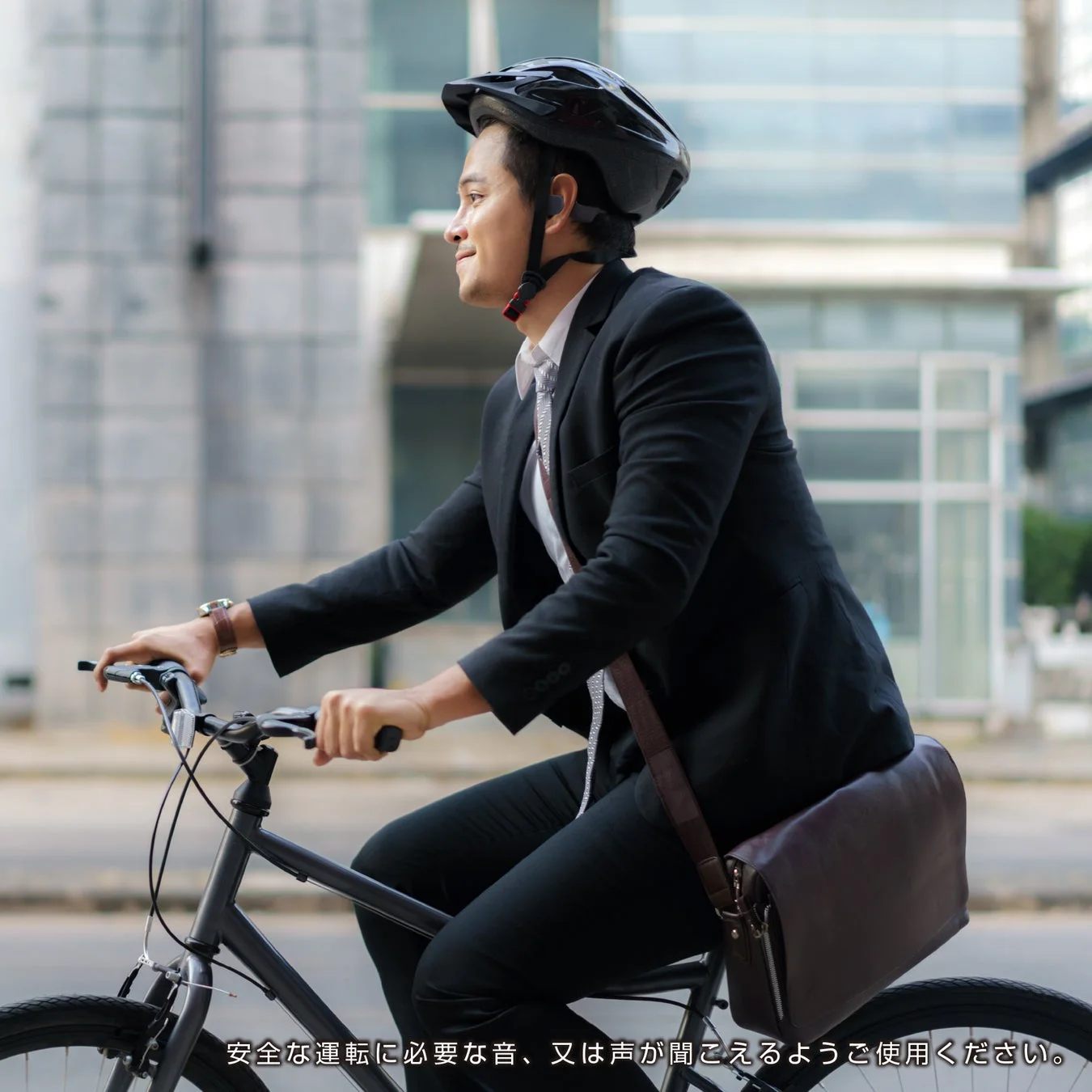 スーツ姿のビジネスマンがヘルメットとイヤホンを着用し、笑顔で自転車に乗っている