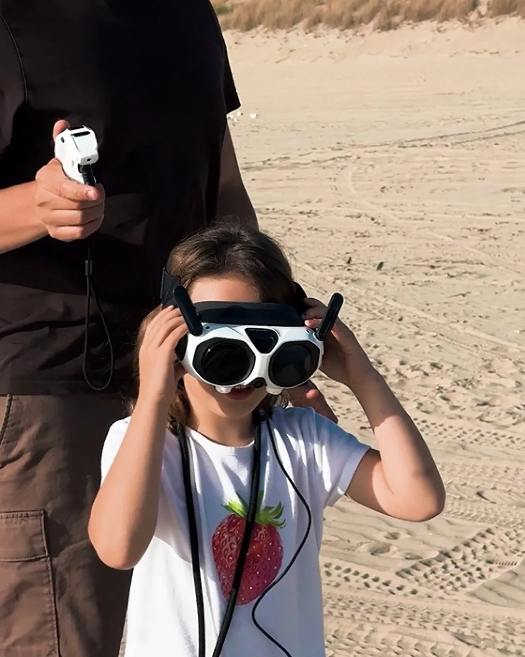 砂浜でFPVゴーグルを装着した子供とドローンコントローラーを持つ大人