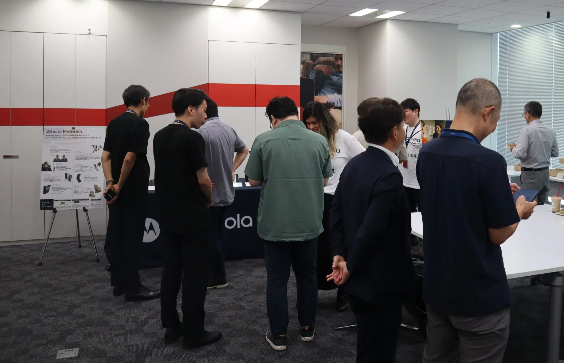 オフィスのような空間で、人々がモトローラ社の歴史やモバイルテクノロジーに関する展示を見ている様子。