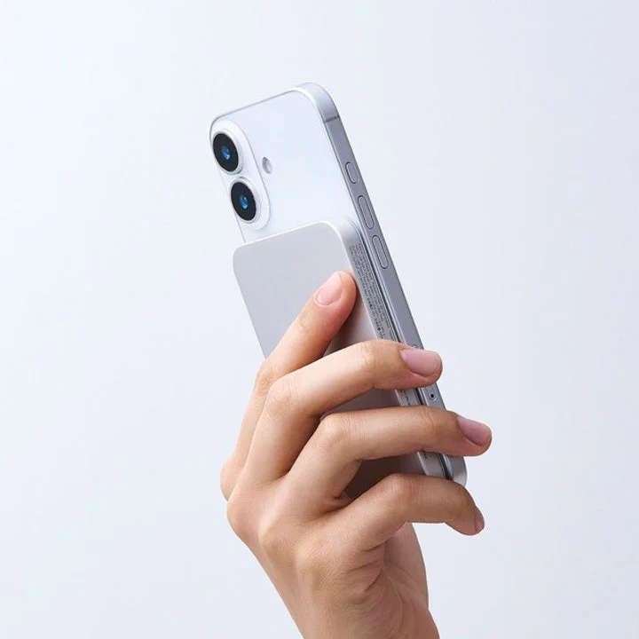 白い背景の前で、手がシルバーのスマートフォンを握っています。スマートフォンの背面には、長方形のモバイルアクセサリーが装着されており、デバイスとアクセサリーのデザインが際立っています。