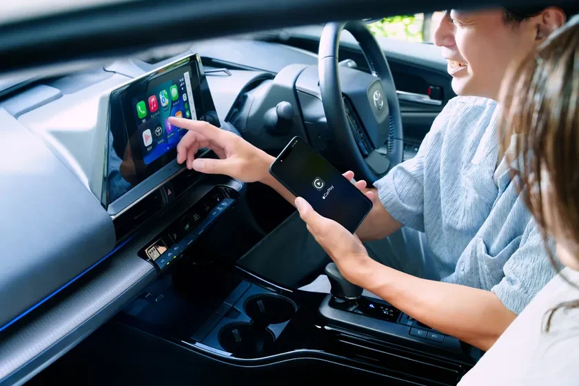 男性が車内でApple CarPlayを介してスマートフォンと接続されたインフォテインメントシステムのタッチスクリーンを操作しています。現代の車内テクノロジーとユーザー体験を示唆する一枚です。