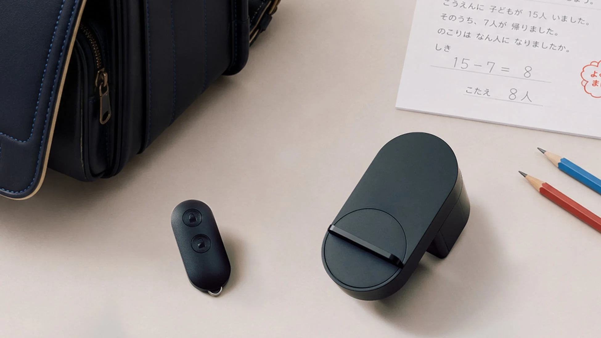 ランドセル、スマートロック、リモコン、鉛筆、そして算数の宿題が置かれた机の上の様子