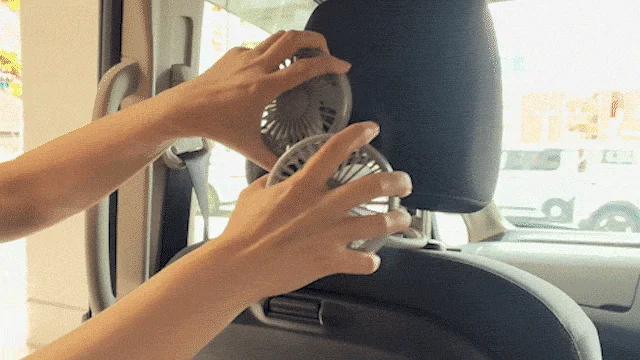 車のヘッドレストに2つのポータブル扇風機を取り付けている様子です。車内を涼しく快適にするためのアイテムで、特に夏のドライブに役立ちそうです。
