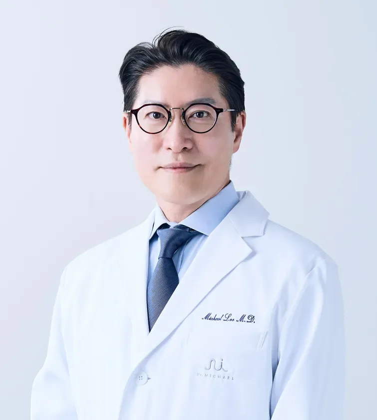 白衣と眼鏡を着用したアジア系の男性医師のポートレート。カメラをまっすぐ見つめており、専門的で信頼感のある印象を与えます。
